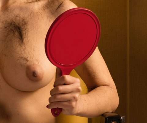Detail einer Fotografie: Weibliche Brust mit Haaren und Handspiegel