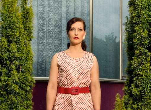 Frau mit rot gepunktetem Kleid und strengem Blick.