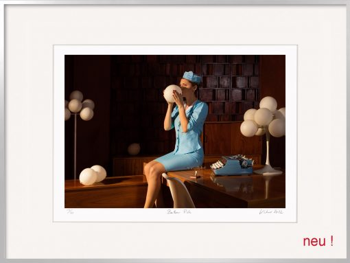Horst Kistner Balloon Ride Fotografie ist inszeniert. Die surreale Szene spielt in einem Büro. Eine elegant gekleidete Frau sitzt auf dem Schreibtisch neben einer Schreibmaschine. Sie hält einen weißen, runden Glas Lampenschirm in der in den Händen und versucht diesen aufzublasen.
