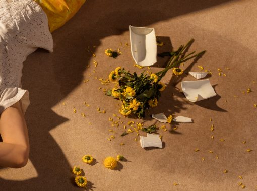 Eine Detailaufnahme von Horst Kistner Failure Fotografie zeigt eine zerbrochene Blumenvase neben einer auf dem Teppich liegenden Frau.