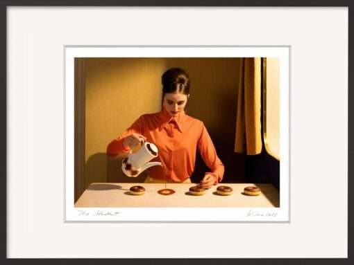 Frau in orangefarbener Bluse gießt Kaffee auf den Tisch neben Donuts – Fotografie The Student von Horst Kistner, originelles Geschenk und Kunst für die Küche im Vintage-Stil