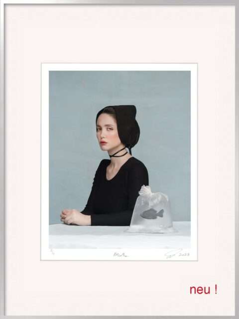 Die Fotografie von Somy Samani Breathe zeigt eine junge Frau im Profil, die an einem Tisch sitzt. Sie trägt ein schlichtes schwarzes Kleid und eine schwarze Haube, die an historische oder religiöse Kleidung erinnert. Ihr Blick ist ernst, beinahe stoisch, gerichtet auf den Betrachter, während ihr Körper zur Seite gewandt ist. Um ihren Hals liegt ein schwarzes Band.