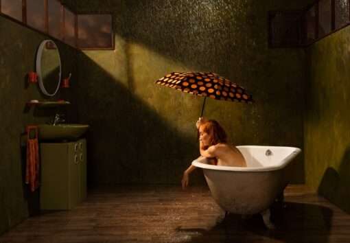 Eine Frau mit Regenschirm in Badewanne während Regen – Fotografie Monsun von Horst Kistner. Inszenierte Fotografie aus Soll und Haben zu kaufen.