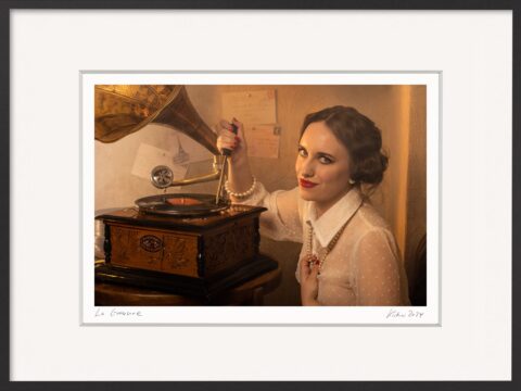 Frau mit rotem Lippenstift und schelmischem Blick ritzt mit einem Dorn in eine Schallplatte – Fotografie „Die Rebellion der Frau“ von Horst Kistner. Sinnbild für starke, selbstbewusste Frauen – perfekte Geschenkidee im kleinen Format.