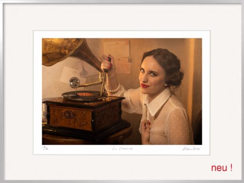 Frau mit rotem Lippenstift, Perlenkette und schelmischem Blick vor einem Grammophon – sie ritzt mit einem Dorn in die Schallplatte. Horst Kistners Fotografie La Gravure zeigt böse Frauen in der Kunst als kluge, selbstbewusste und ironische Heldinnen – eine surreale Hommage und ideales Geburtstagsgeschenk für Frauen mit Sinn für Stil.