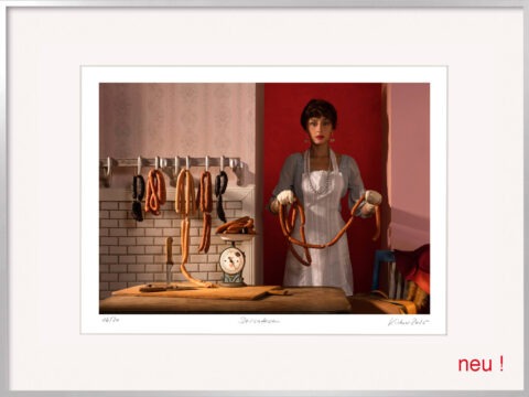 Limitierte Delicatessen Fotografie von Horst Kistner im silbernen Alu-Rahmen. Surreale Küchenfotografie mit Frau, Wurstketten und intensiver roter Wand.